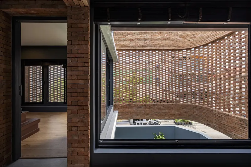 Interior view through glazed openings to a perforated brick wall screening a courtyard with planted beds below