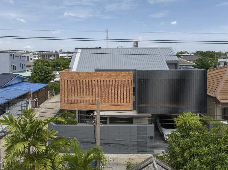 Elevated view of the perforated brick screen and corrugated metal roof volumes above a residential neighborhood