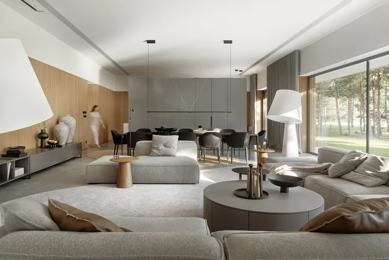 Open living and dining space with floor-to-ceiling glazing overlooking the wooded landscape beyond