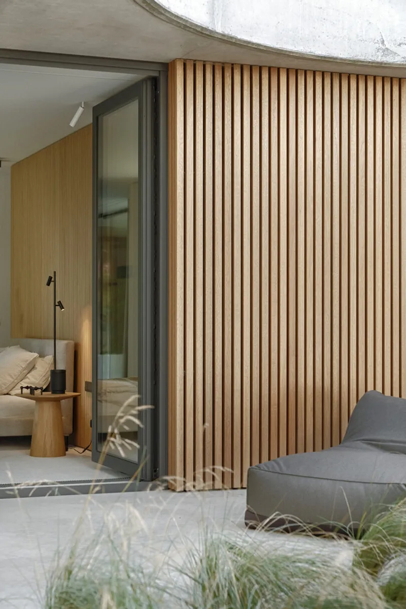 Vertical timber screen beside a sliding glass door opening to a bedroom with planted grasses in foreground