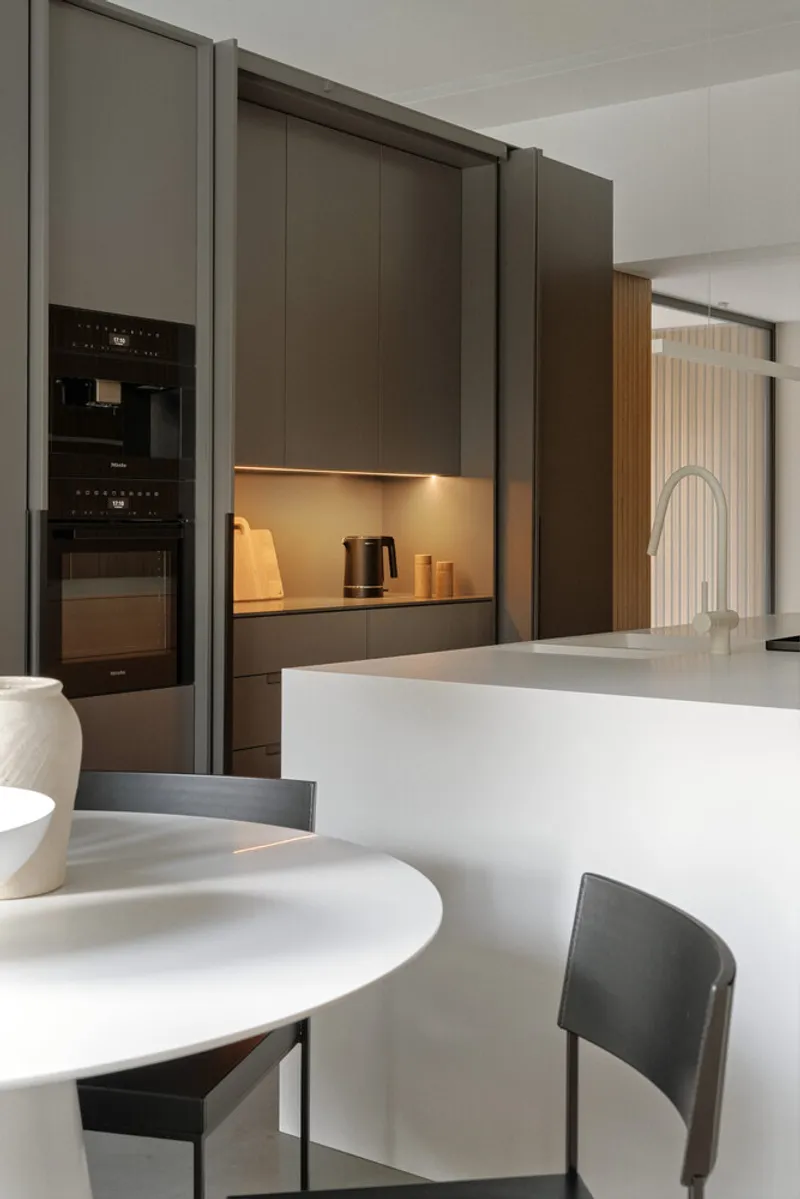 Kitchen view showing dark cabinetry with integrated backlighting and a white marble island with dining table