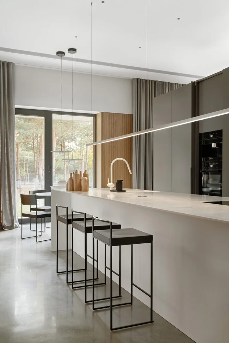White kitchen island with bar stools and linear pendant light beneath a recessed ceiling slot