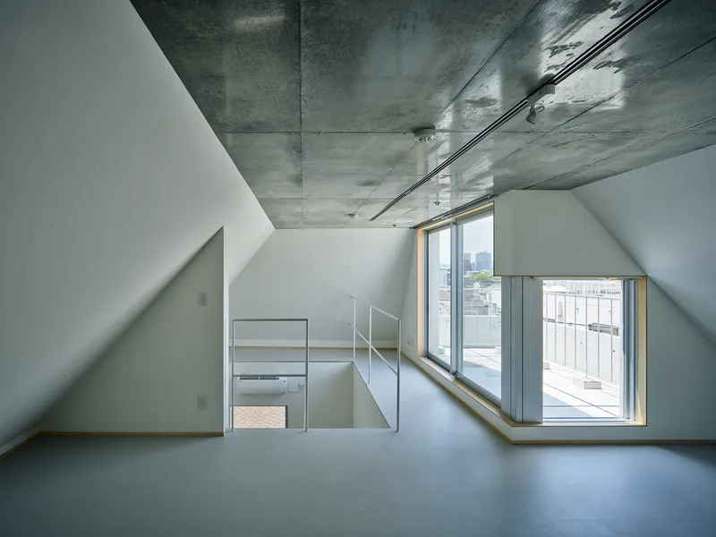Upper floor interior with exposed concrete ceiling, white walls, and angled windows overlooking neighboring rooftops