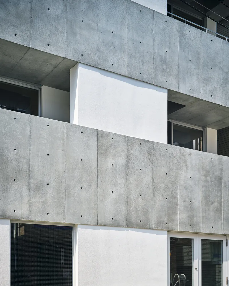 Close-up of the concrete facade with recessed white balcony panels and exposed tie holes in daylight