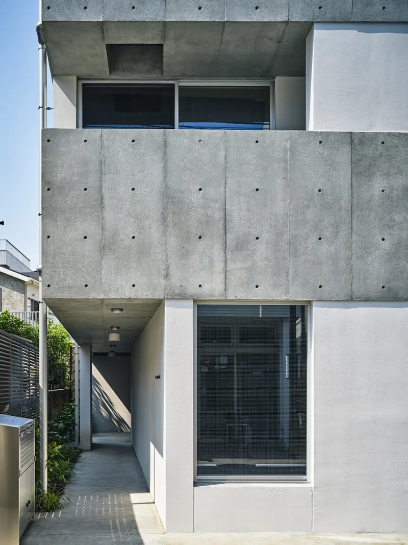 Side entry path leading under cantilevered concrete slabs with planted bed and horizontal timber fence