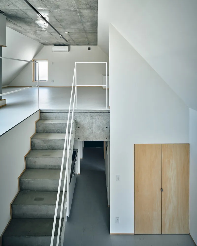 Split-level interior showing concrete stairs with white railing connecting floors beneath an exposed concrete ceiling