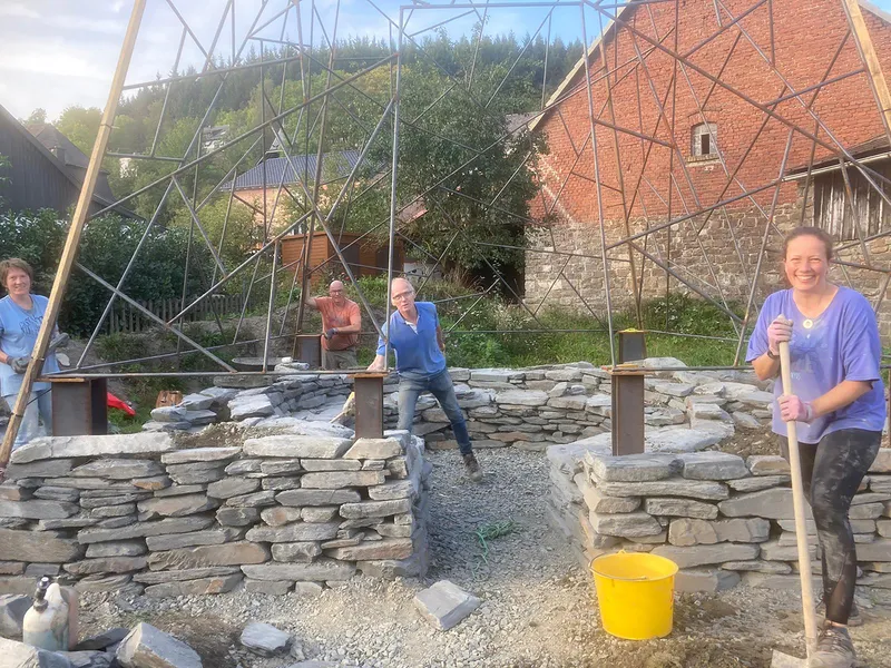 View through the triangulated frame showing circular dry-stone walls and builders during construction