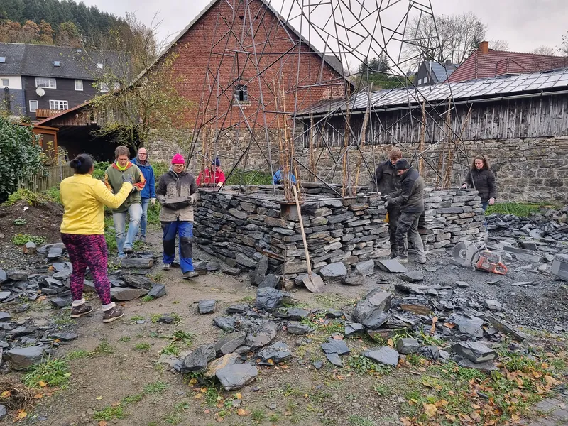 Community group assembling the dry-stone walls beneath the triangulated metal frame in autumn
