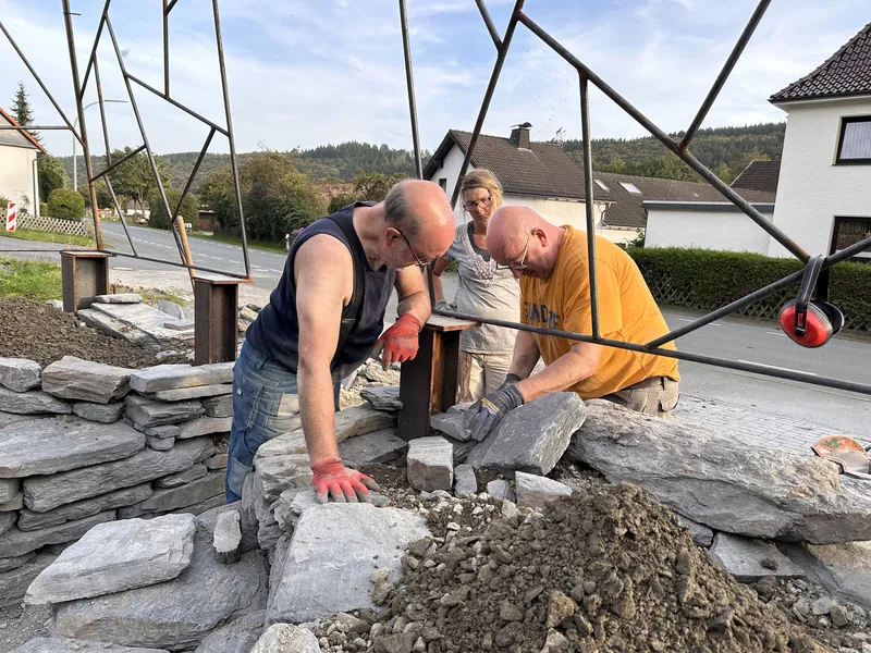 Three builders laying slate stones through the triangulated metal frame onto the circular base