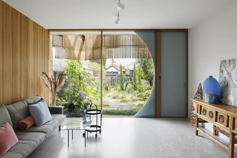 Living room with circular portal framing a garden view through timber slat screens