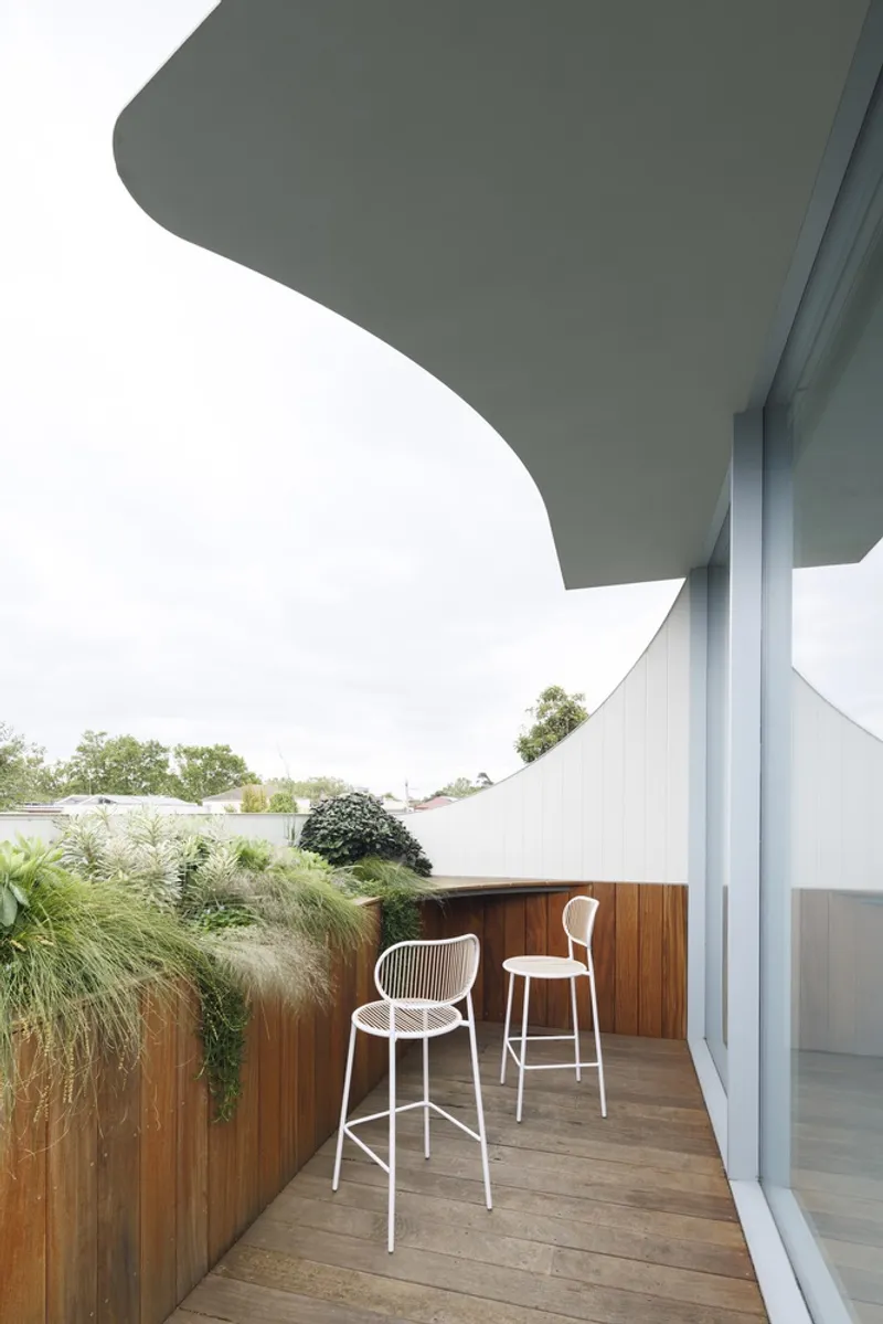 Timber-clad balcony with two bar stools beneath a curved roof overhang