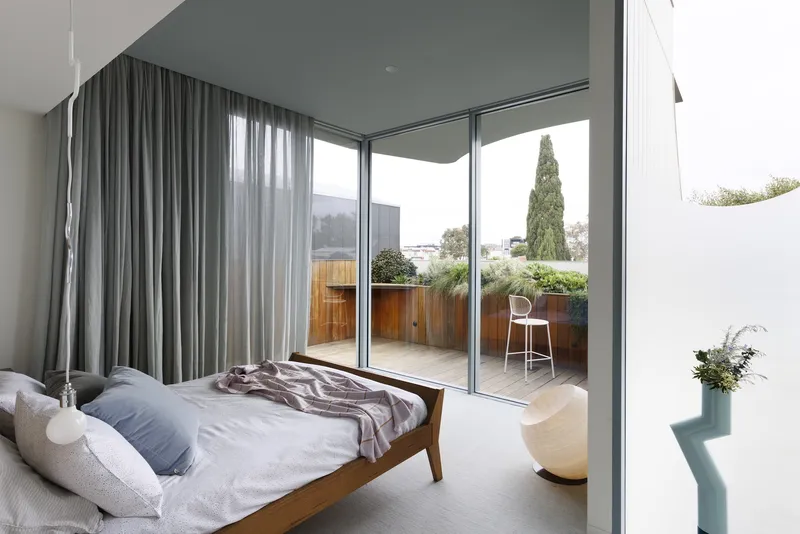 Bedroom with floor-to-ceiling glazing opening onto a terrace with timber screening and planted pots