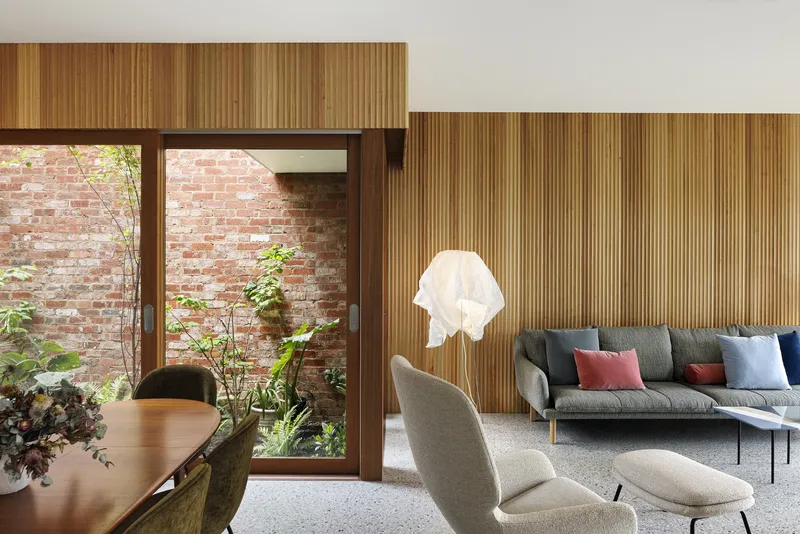 Timber-battened wall with doorway framing a courtyard and exposed brick