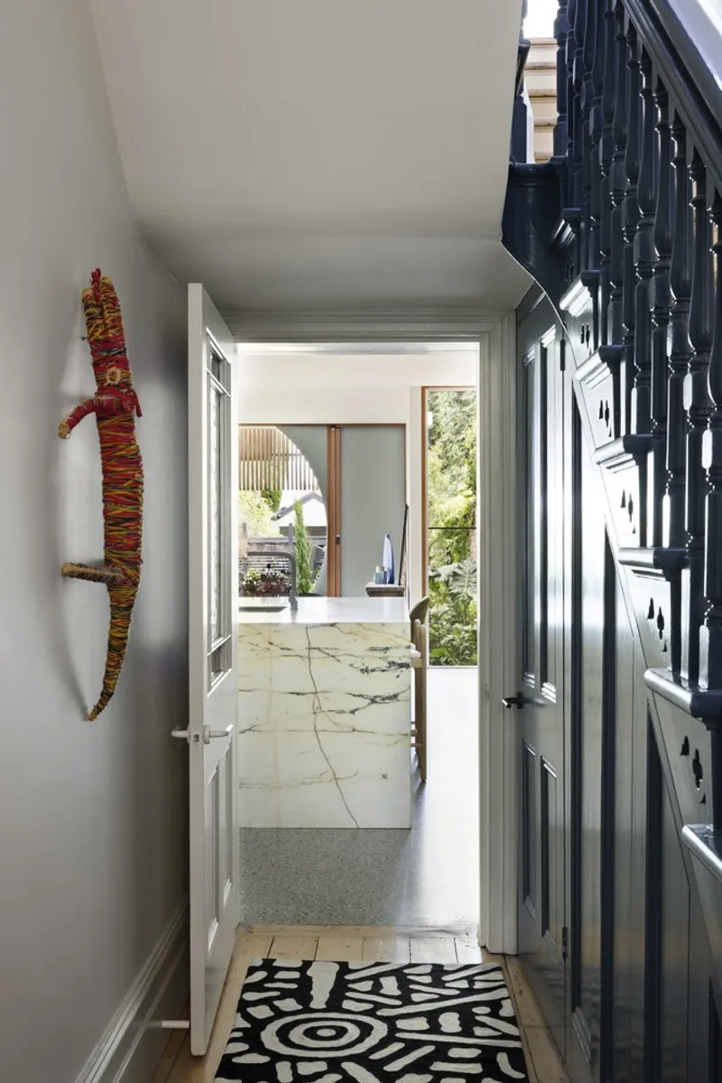 Entry hallway with patterned floor mat and open door revealing stone paving and greenery beyond