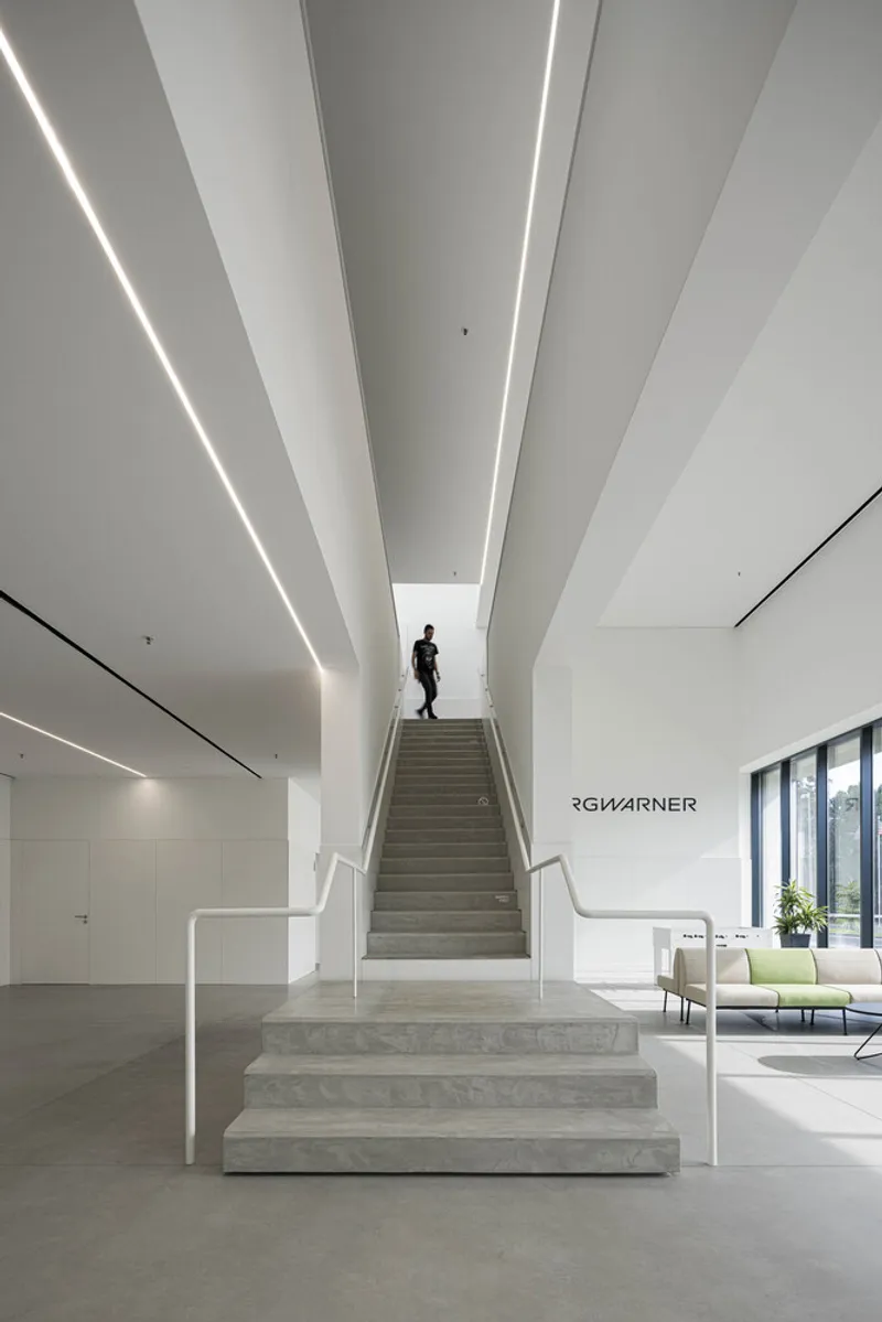 Concrete staircase with angular ceiling beams and linear lighting leading to upper floors