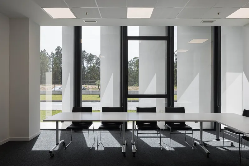 Interior conference room with white surfaces, tall vertical windows, and recessed ceiling panels