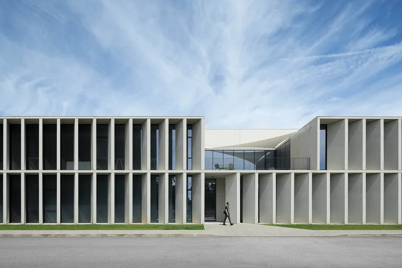 Street view of the ribbed concrete facade with vertical fins and a person walking toward the entrance