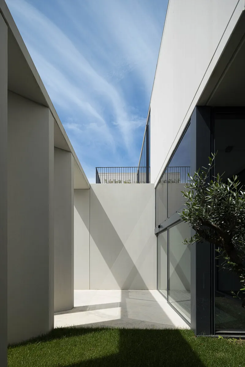 Courtyard view framed by white walls and full-height glazing with lawn and blue sky above