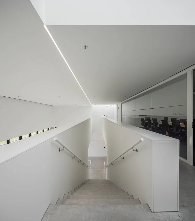 Top-down view of a descending staircase flanked by white walls and linear ceiling lighting