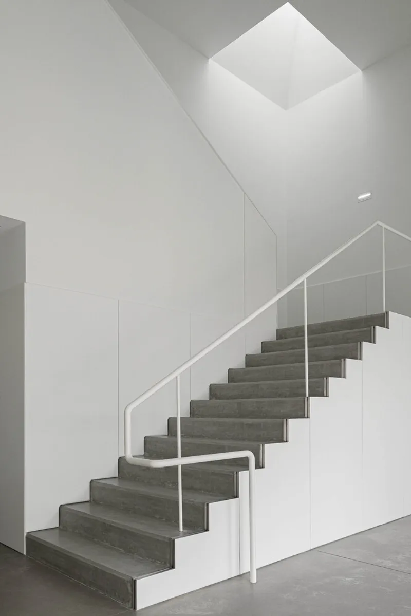 Interior staircase with dark treads and white tubular handrail beneath a square skylight