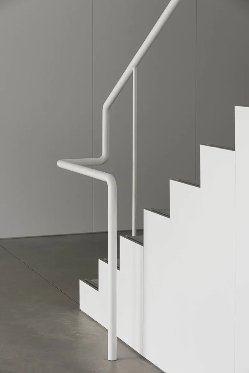 Detail of white tubular steel handrail bending around the staircase corner