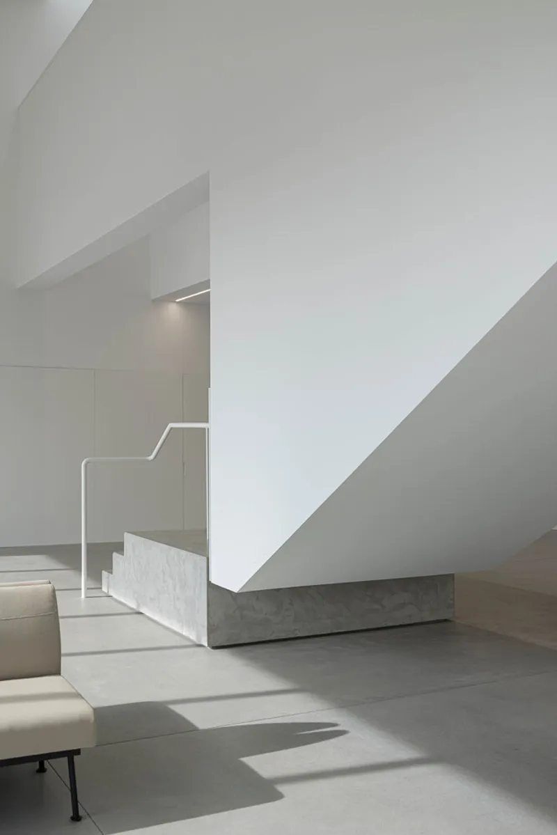 View of staircase base with angular white walls and linear skylight illuminating the marble treads