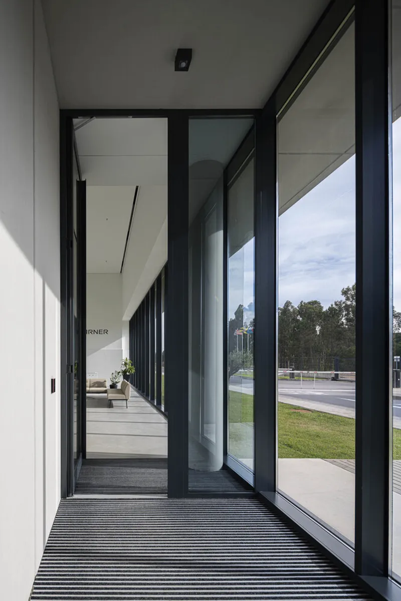 Covered entrance with black aluminum glazing and ribbed matting overlooking lawn and distant trees