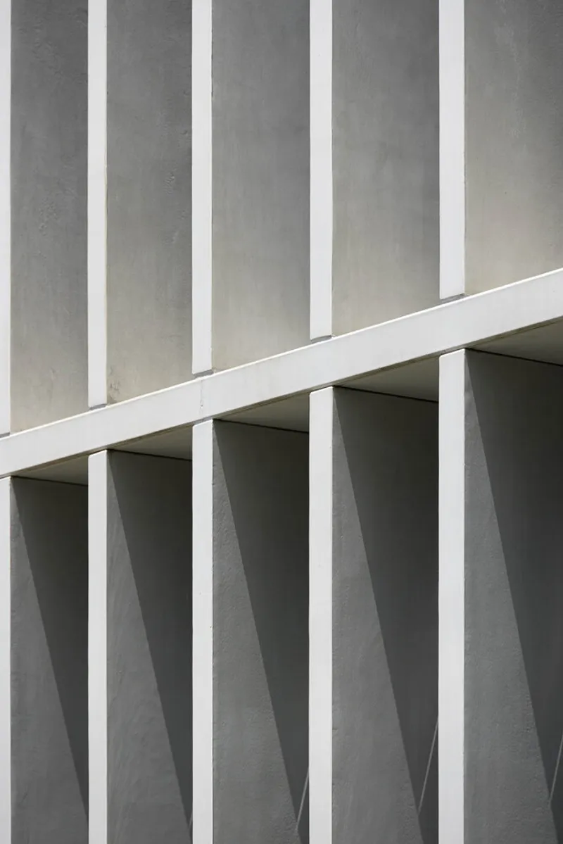 Facade detail showing vertical white fins alternating with deep recessed openings in concrete