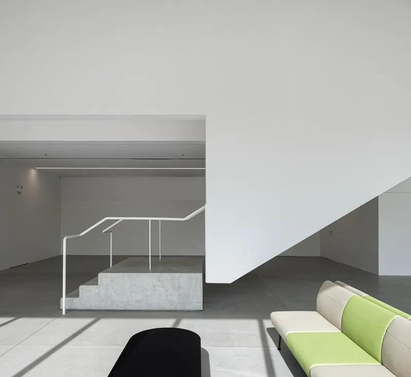 Concrete staircase with white handrail beside a seating area with green cushions in morning sunlight