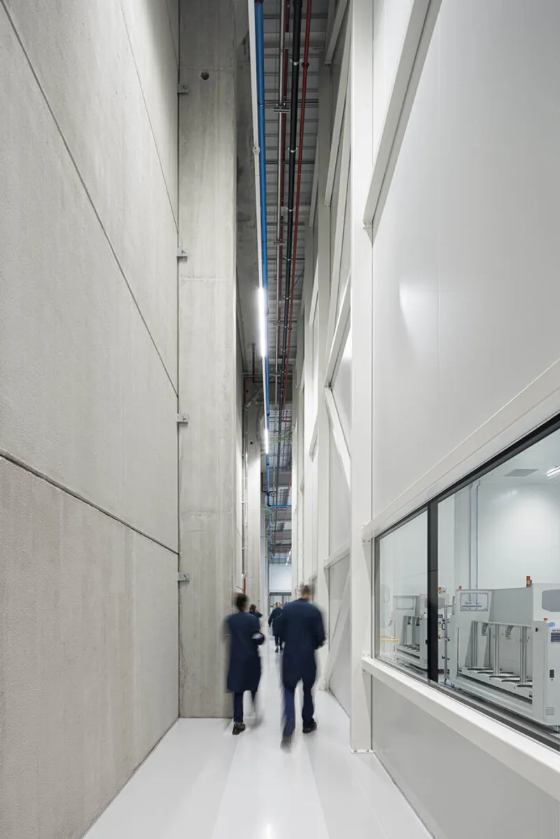 Interior corridor with exposed mechanical ceiling and two blurred figures walking past glazed lab spaces