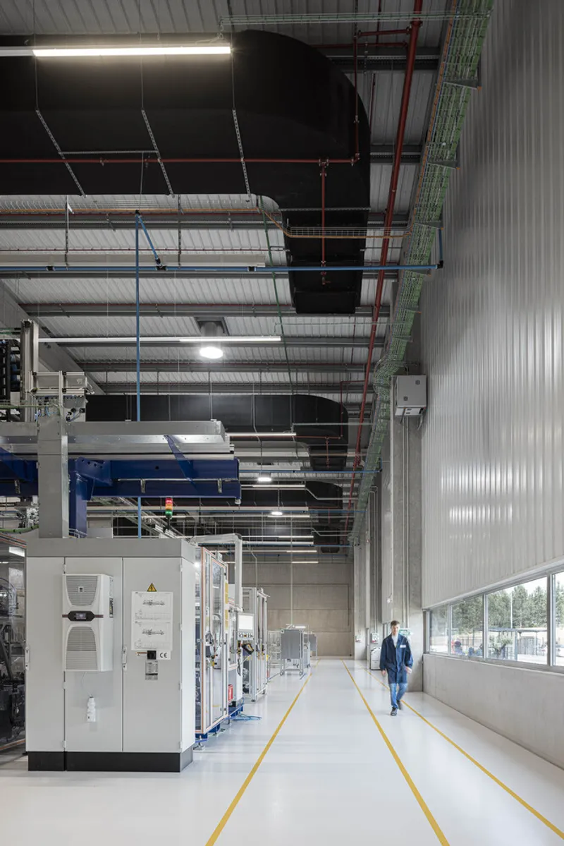 Production floor with exposed ceiling ducts, machinery, and corrugated metal wall panels alongside a person in blue