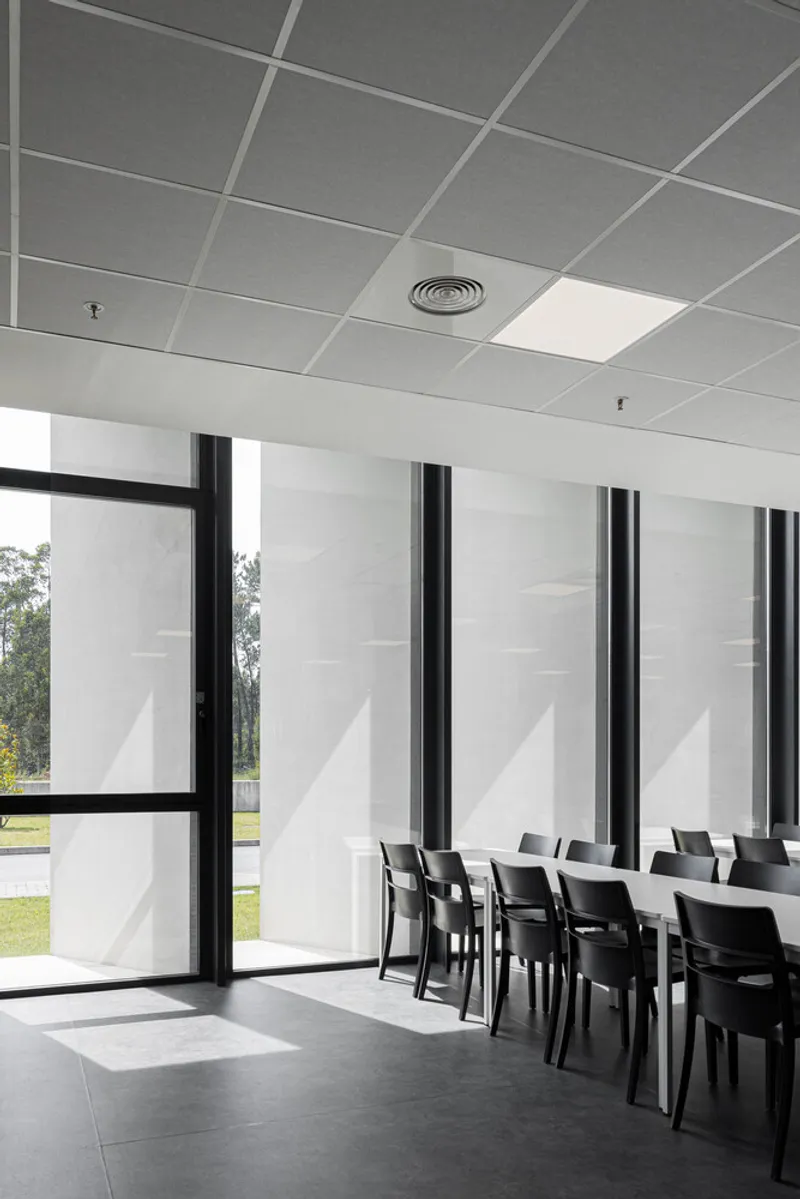 Dining area with rows of chairs along window wall beneath acoustic ceiling tiles and circular diffuser