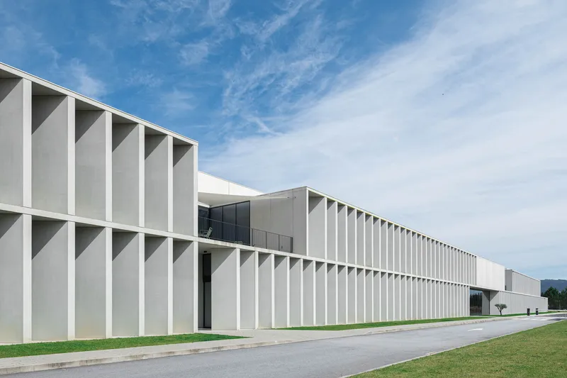 Long facade with vertical fin system in white concrete under blue sky with distant mountains