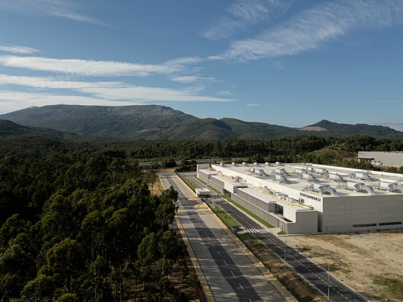 Aerial view of the factory complex set between forested hillsides and distant mountains
