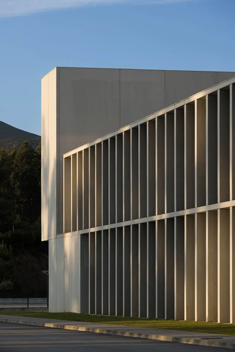 Facade detail with vertical concrete fins wrapping the corner against a mountain backdrop at dusk