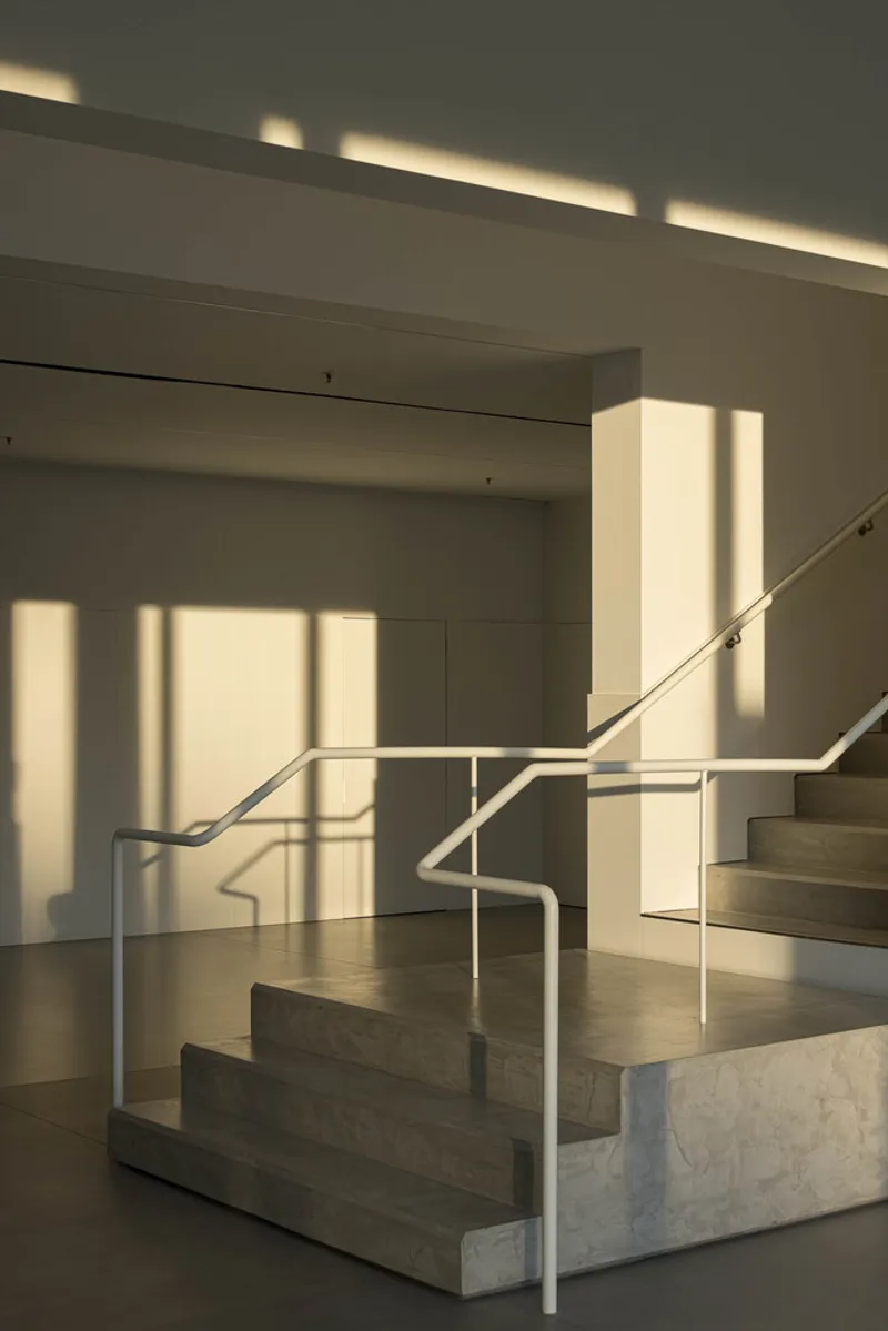 Interior staircase with metal handrails bathed in afternoon light casting geometric shadows on white walls