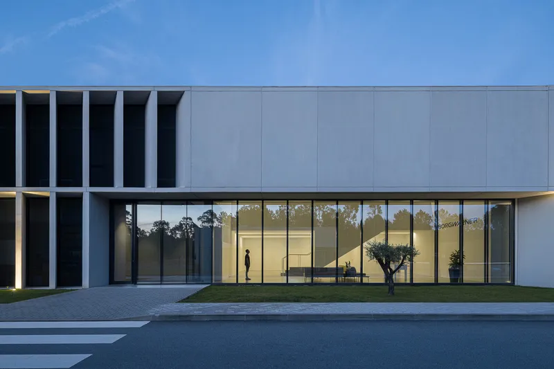 Main entrance with floor-to-ceiling glazing revealing a figure inside the illuminated foyer at dusk