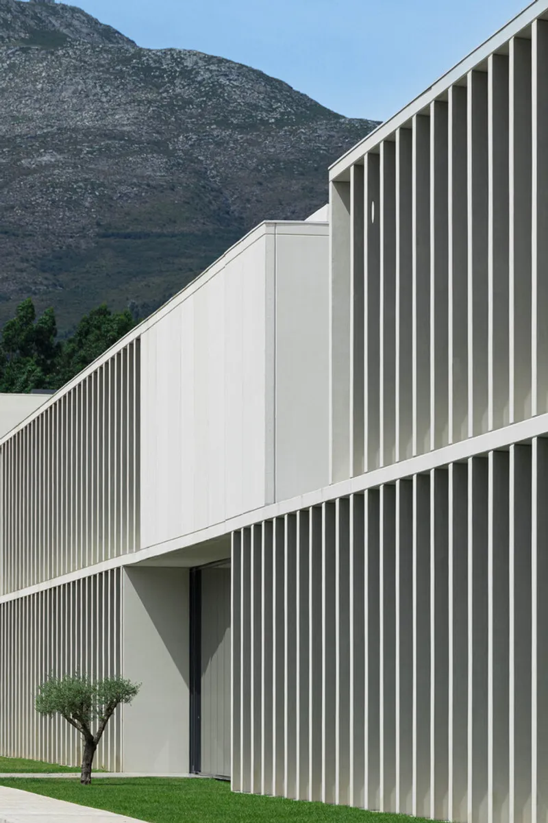 Angled view of the white vertical louver facade with a small tree against a mountain backdrop