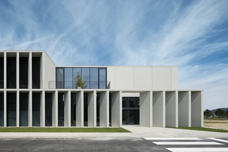 Entry courtyard with vertical concrete fins and a glazed upper volume beneath cirrus clouds
