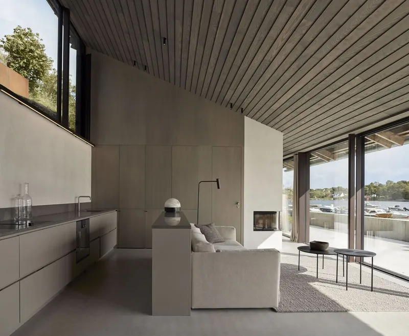 Open plan living space with wood slat ceiling and floor-to-ceiling glazing facing the water