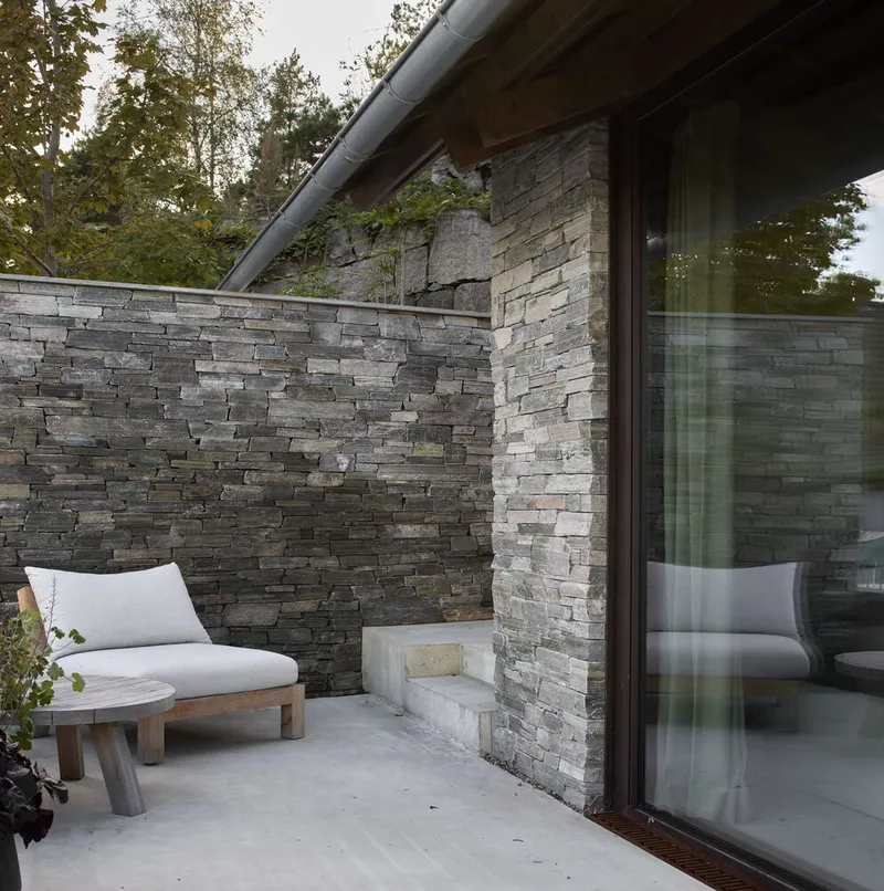 Exterior terrace with concrete floor and stacked stone wall enclosing seating beneath a metal roof