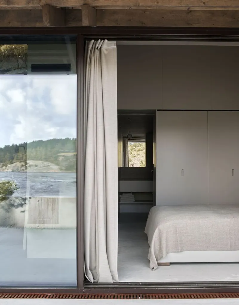 Bedroom with floor-to-ceiling glazing, linen curtain and view toward the forested waterfront