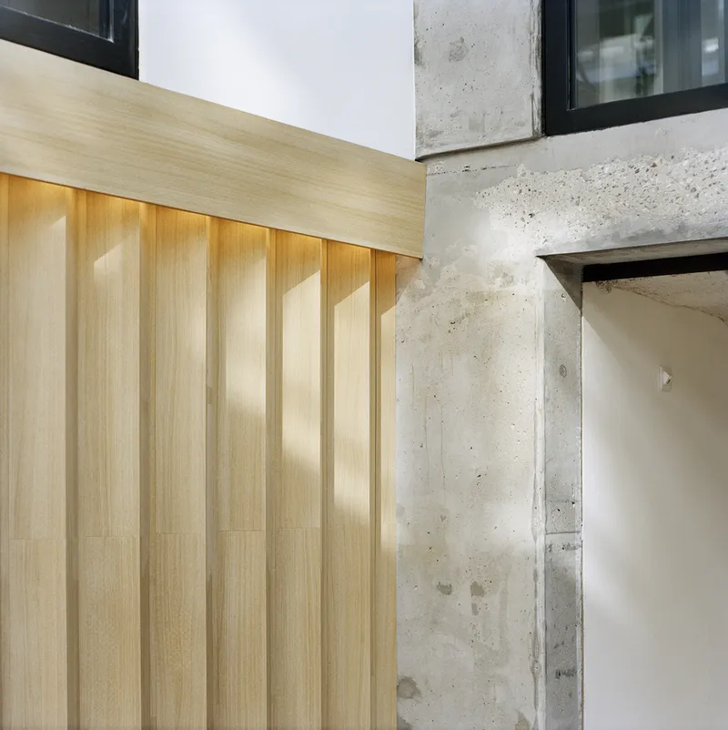 Detail of vertical timber paneling meeting raw concrete column with light washing across the surfaces
