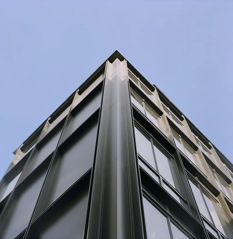 Upward view of metal-clad corner facade with horizontal window bands against pale sky