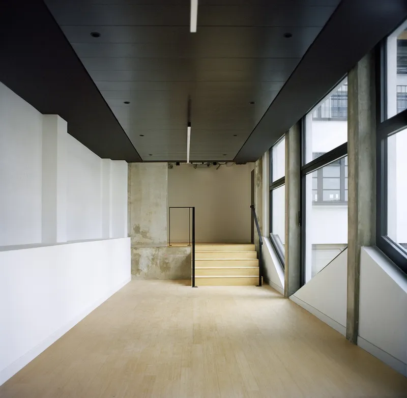 Interior hallway with black ceiling plane and timber staircase ascending alongside floor-to-ceiling windows