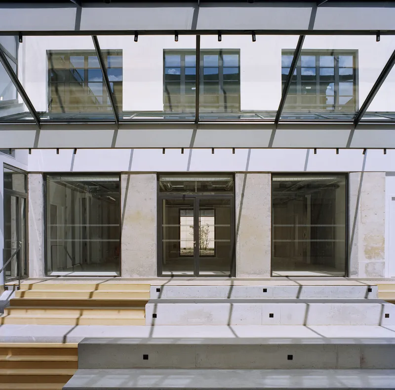 Courtyard view of tiered stone seating beneath a glazed canopy looking toward the interior glazing