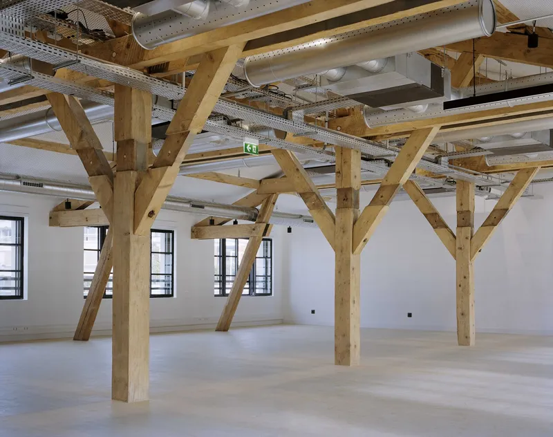 Interior space showing diagonal timber trusses with exposed mechanical ducts and linear lighting above pale floors