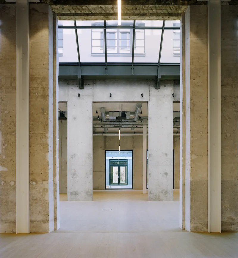 Axial view through concrete columns and doorways with exposed ceiling ducts and clerestory glazing