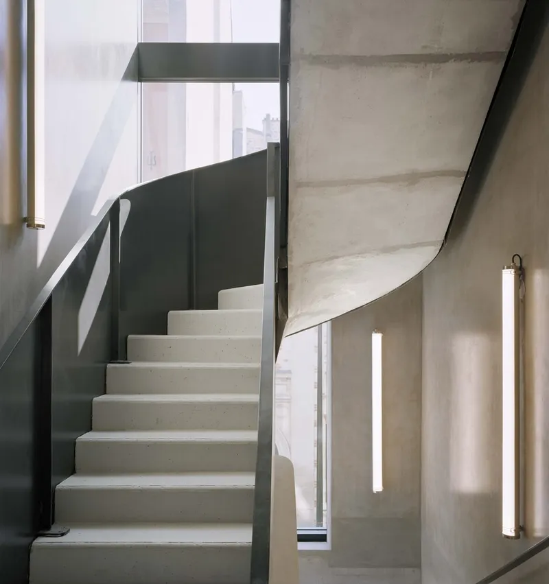 Precast concrete staircase curving upward with dark metal balustrade and vertical strip lighting