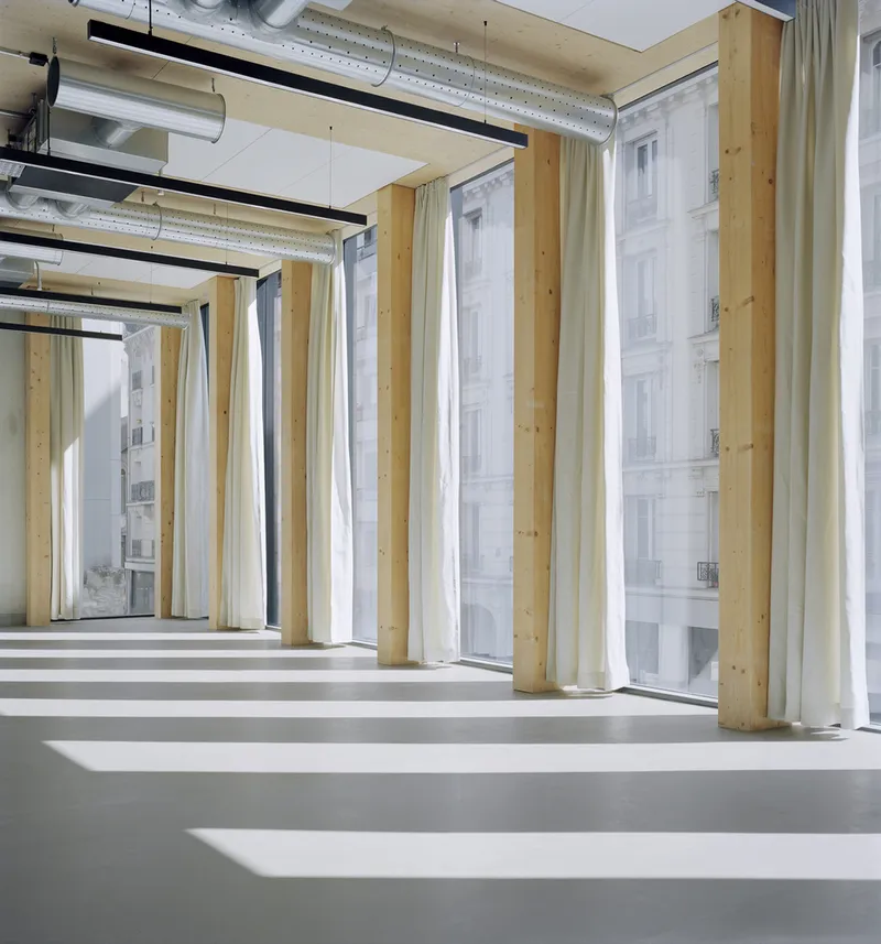Open-plan office space with timber columns, exposed ductwork and afternoon light striping the floor